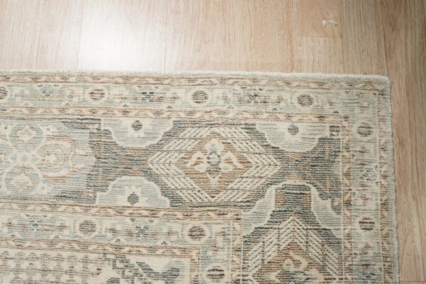 Distressed cream, blue, brown, and gray patterned rug corner on light wood plank flooring.