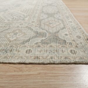 Low-angle view of a plush, traditional rug in cream, blue-grey, and tan on light wood planks.