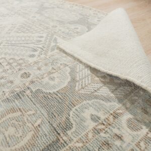 Distressed round rug in gray, brown, and cream with the woven backing visible on light wood planks.