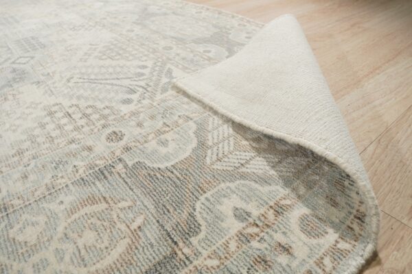 Distressed round rug in gray, brown, and cream with the woven backing visible on light wood planks.