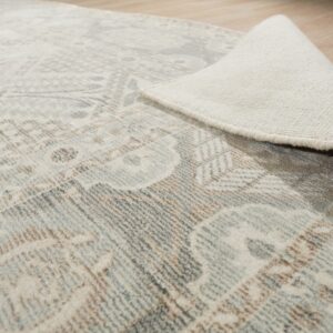 A cream, gray, and brown patterned rug is rolled back, exposing its backing on light wood flooring.