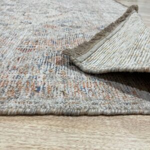 A textured low-pile rug with orange and blue accents is folded over on light wood flooring.