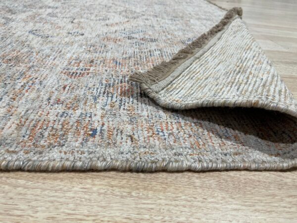 A textured low-pile rug with orange and blue accents is folded over on light wood flooring.