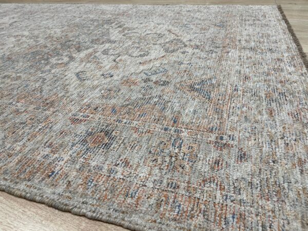 Textured high-pile rug with faded traditional patterns in gray, cream, rust, and blue rests on wood flooring.