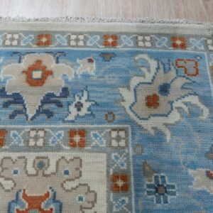 Blue, cream, and rust traditional rug with dense pile shown on light wood planks.