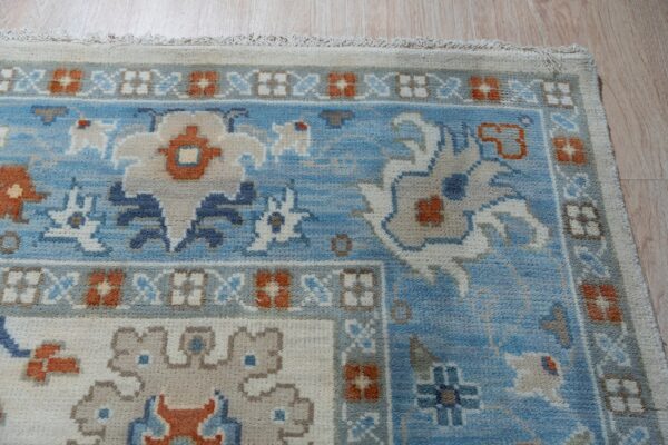 Blue, cream, and rust traditional rug with dense pile shown on light wood planks.