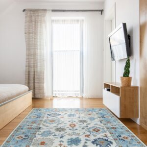 Traditional blue, beige, and terracotta rug on hardwood floor in a brightly lit bedroom with light wood furniture.