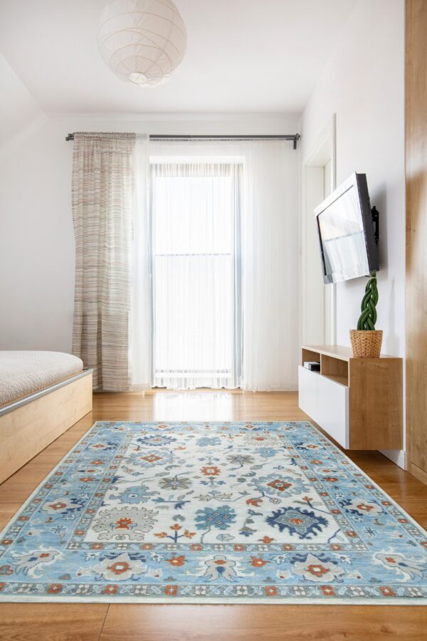 Traditional blue, beige, and terracotta rug on hardwood floor in a brightly lit bedroom with light wood furniture.