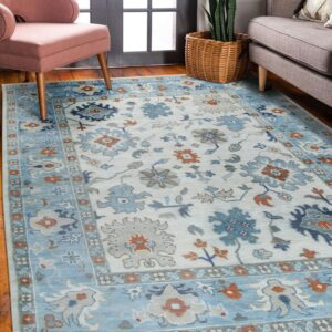 Low-pile rug with blue, cream, gray, and rust floral patterns placed between a chair and sofa.