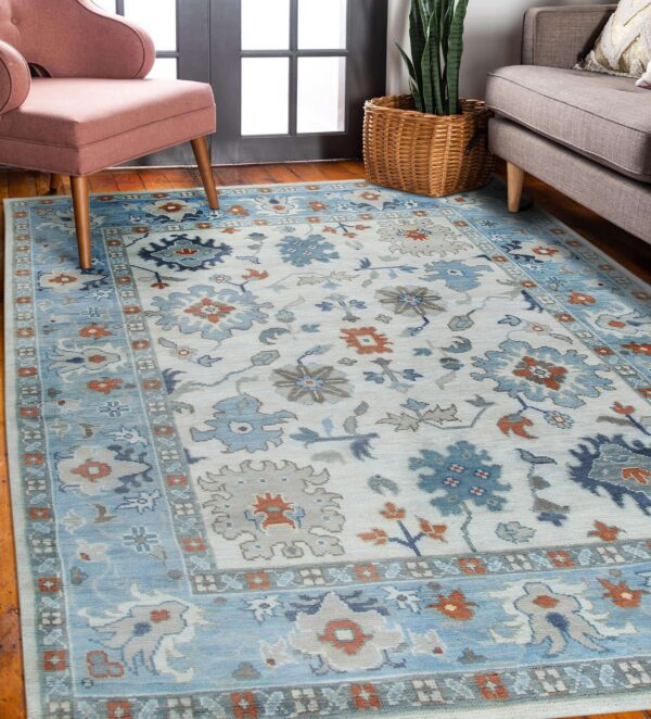 Low-pile rug with blue, cream, gray, and rust floral patterns placed between a chair and sofa.