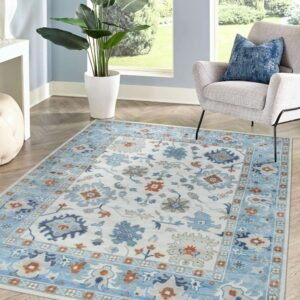 Traditional blue, cream, and orange floral rug in a bright room with a gray chair and wood floor.