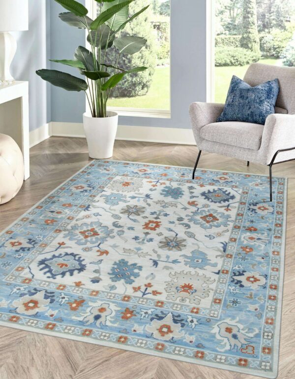 Traditional blue, cream, and orange floral rug in a bright room with a gray chair and wood floor.