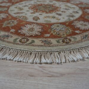Round cream and rust floral rug with fringe, resting on light wooden plank flooring.