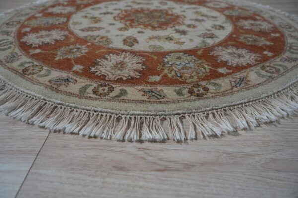 Round cream and rust floral rug with fringe, resting on light wooden plank flooring.