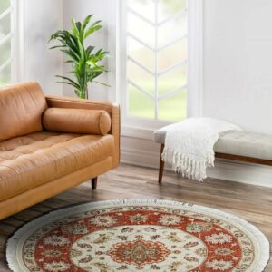 Round rust and cream patterned rug resting on wood floors beside a leather sofa and upholstered bench.