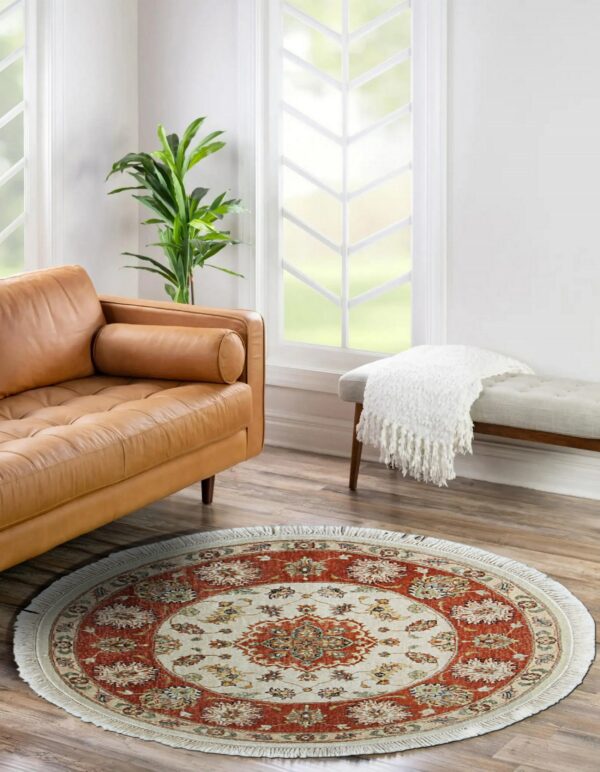 Round rust and cream patterned rug resting on wood floors beside a leather sofa and upholstered bench.