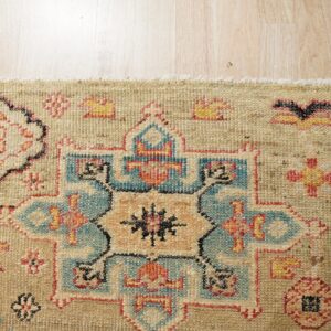 Textured beige rug featuring blue, rust, and yellow geometric motifs displayed on light wood flooring.