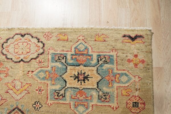 Textured beige rug featuring blue, rust, and yellow geometric motifs displayed on light wood flooring.