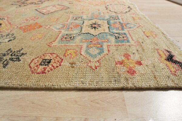 Textured beige rug with blue, orange, pink, and yellow geometric designs, resting on light wood floorboards.