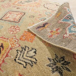 Beige low-pile rug with colorful motifs is folded back, revealing its woven underside on a wood floor.