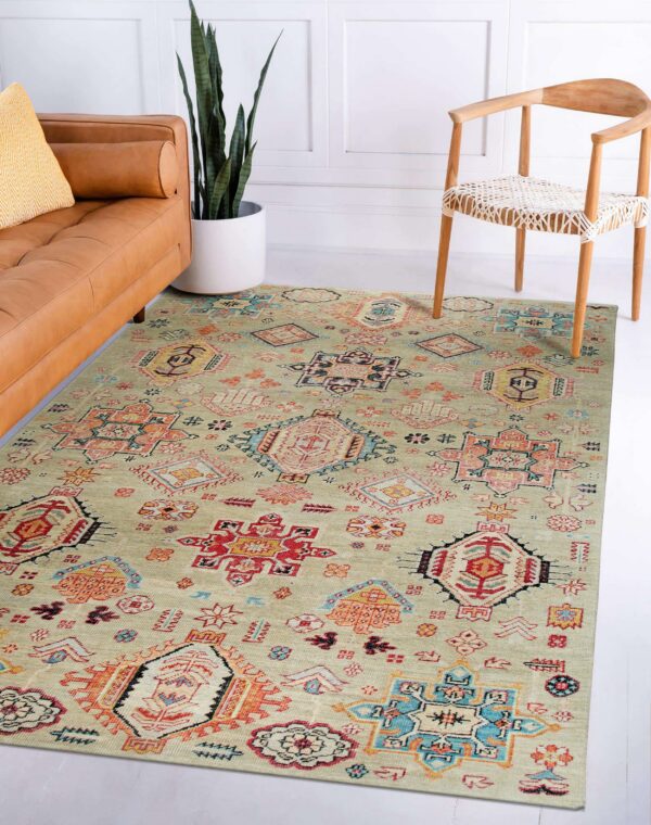 Geometric sage rug with tribal designs lies between a cognac leather sofa and a wooden chair.