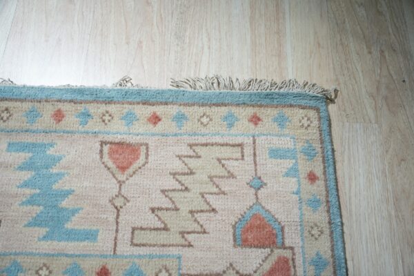 Beige rug with blue and coral geometric designs and fringe on light wood plank flooring.