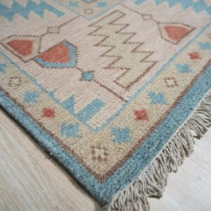 Thick pile rug in pink, light blue, and tan geometric designs rests on pale wood flooring.