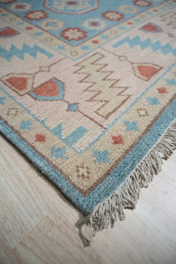 Thick pile rug in pink, light blue, and tan geometric designs rests on pale wood flooring.