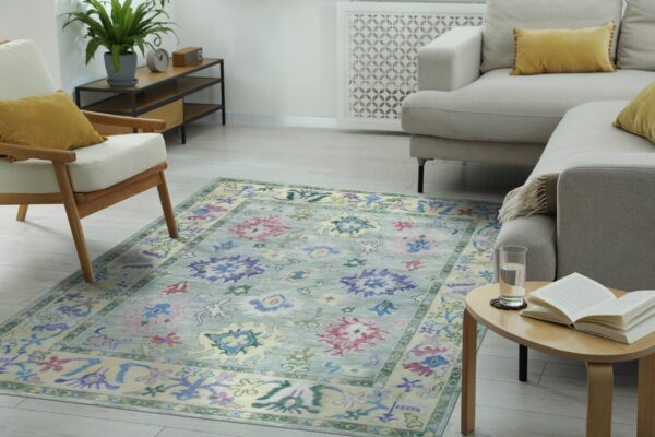 Transitional blue and multicolored patterned rug placed beneath a beige sofa and wooden armchair.