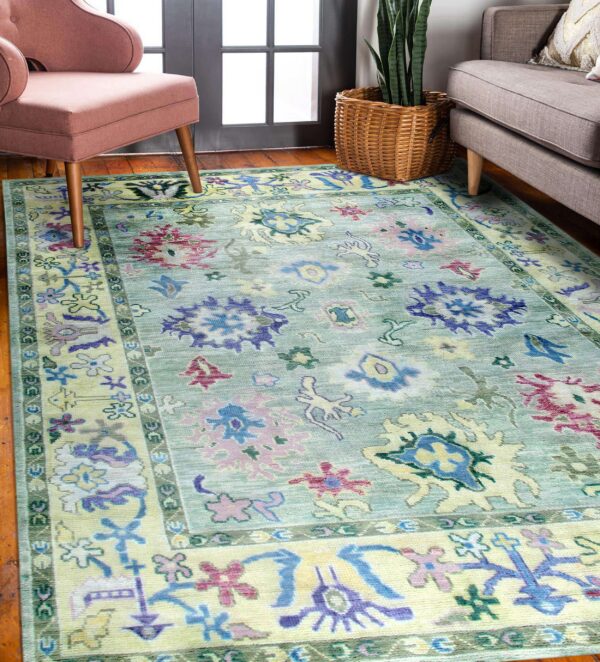 Pale green rug with abstract pink, purple, and yellow motifs sits between a pink chair and gray sofa.