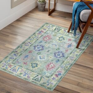 Muted blue-green traditional rug with purple and pink patterns sits on wood plank flooring.