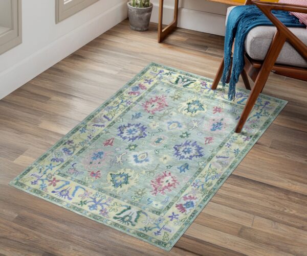 Muted blue-green traditional rug with purple and pink patterns sits on wood plank flooring.
