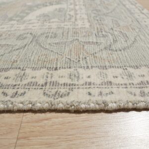 High-pile ivory rug with a muted sage and grey traditional pattern rests on light wood flooring.