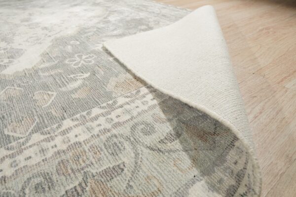 Gray patterned rug rolled back to expose the light woven backing on blonde wood flooring.
