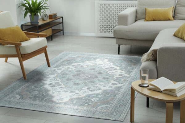 Light blue and grey traditional area rug centered between a beige sofa and a wooden armchair on plank flooring.