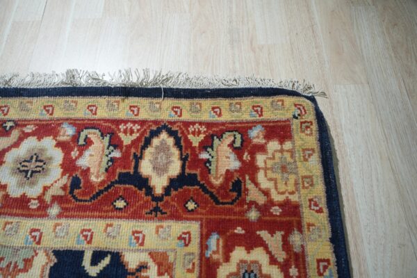Red, navy, and yellow traditional rug with fringe detail lies on light vertical plank wood flooring.