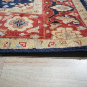 Detail shot of a textured rug border in red, navy, and cream over light wood flooring.