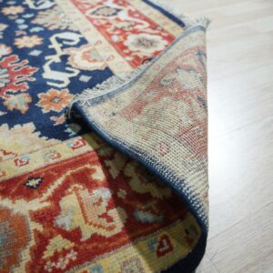 Navy blue and red patterned rug rolled back to show its woven backing on pale wood floors.