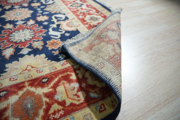 Navy blue and red patterned rug rolled back to show its woven backing on pale wood floors.