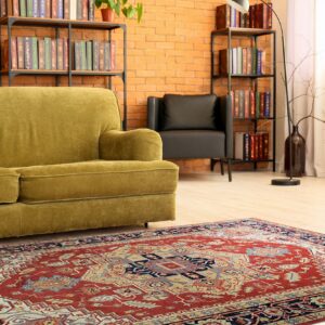 Red and navy traditional area rug beneath a green velvet sofa on light hardwood flooring.