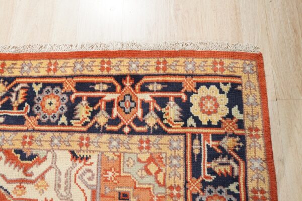Navy, rust, and gold traditional rug border detail with fringe rests on pale wood plank flooring.