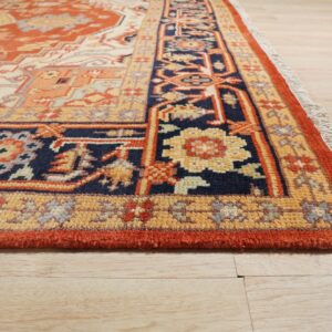 Traditional orange, navy, and gold rug border detail with visible fringe lies on light wood plank flooring.