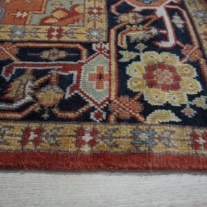 Detailed view of a traditional rug featuring navy, gold, and rust floral patterns resting on light wood floors.