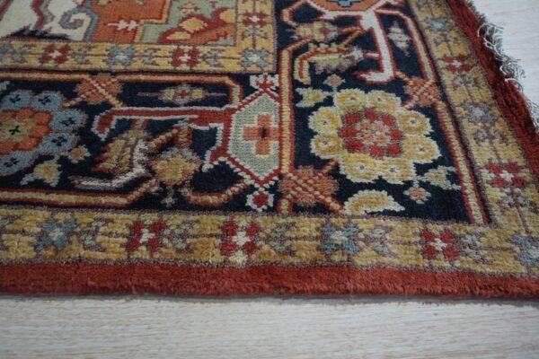 Detailed view of a traditional rug featuring navy, gold, and rust floral patterns resting on light wood floors.