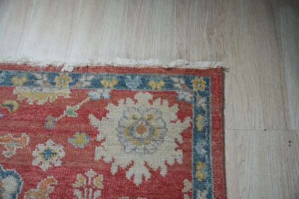 Close-up of a medium pile rug with red, blue, and white traditional floral patterns on light wood flooring.