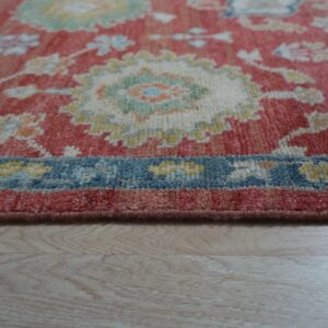 Medium-pile rug detail showing coral, cream, and blue floral patterns resting on light wood flooring.