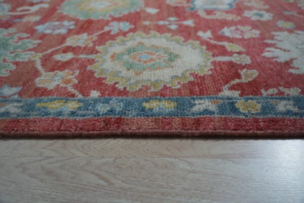Medium-pile rug detail showing coral, cream, and blue floral patterns resting on light wood flooring.