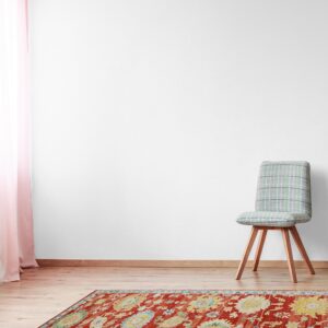 Rusty red rug with colorful traditional medallions on wood floors, beside a gray plaid chair.