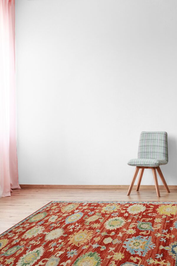 Rusty red rug with colorful traditional medallions on wood floors, beside a gray plaid chair.