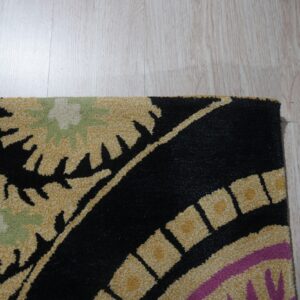 Detail shot of a high-pile rug with black, gold, sage, and magenta patterns on light wood flooring.